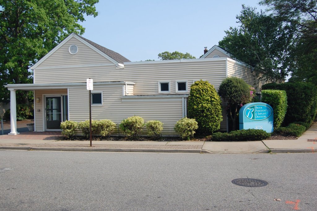 Exterior view of a dental office building with a sign and surrounding greenery